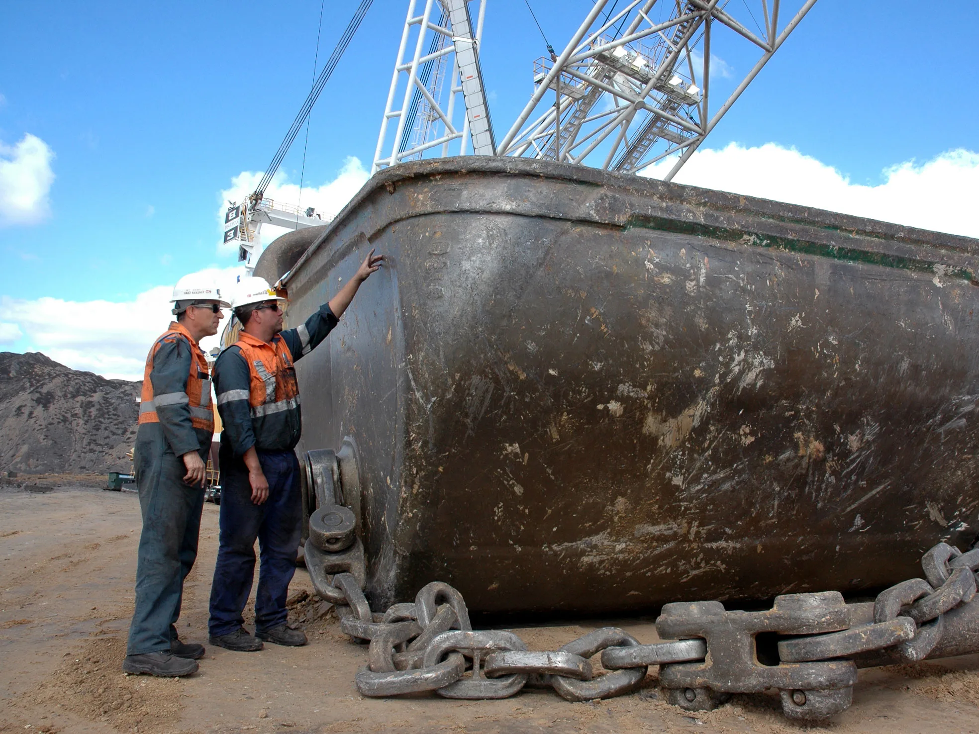 Two mine workers inspecting a large bucket of a dragline